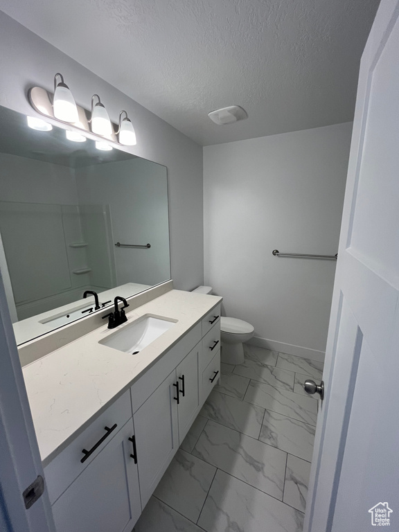 Bathroom with tile floors, vanity with extensive cabinet space, toilet, and a textured ceiling
