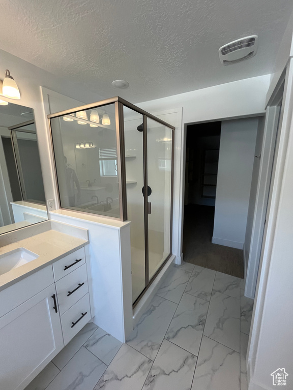 Bathroom with tile flooring, vanity, a shower with shower door, and a textured ceiling
