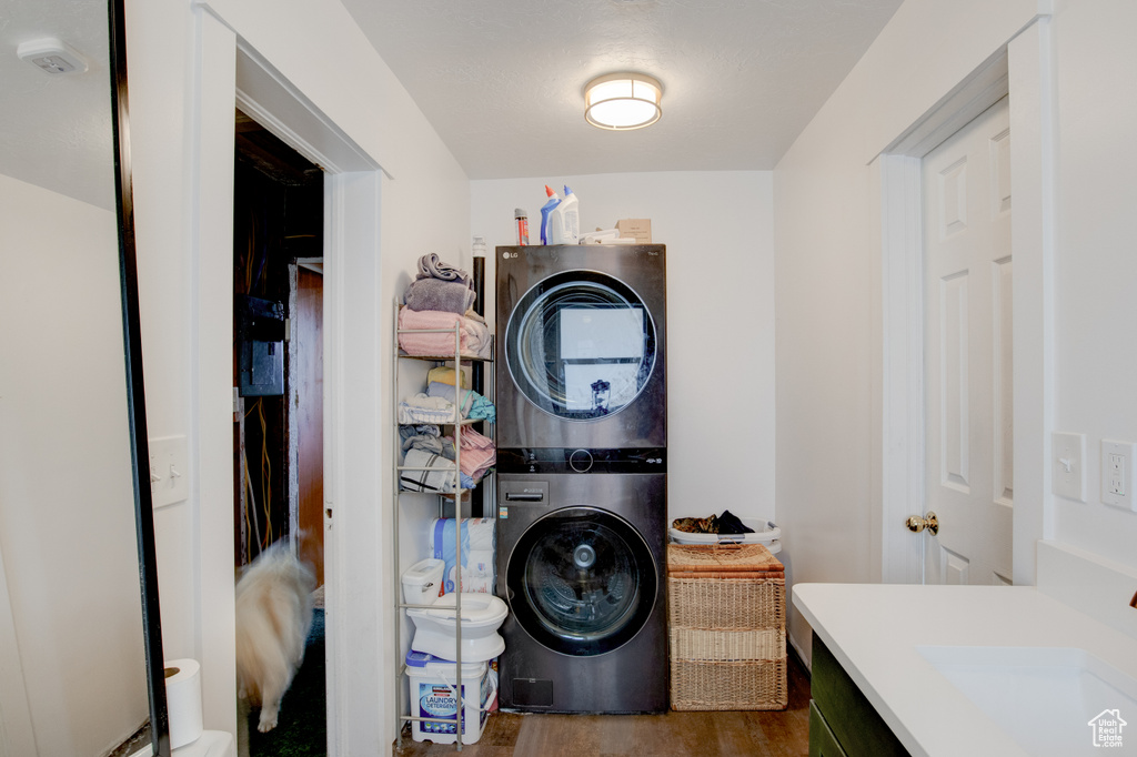 Laundry room featuring dark wood-type flooring, stacked washer and dryer, and sink
