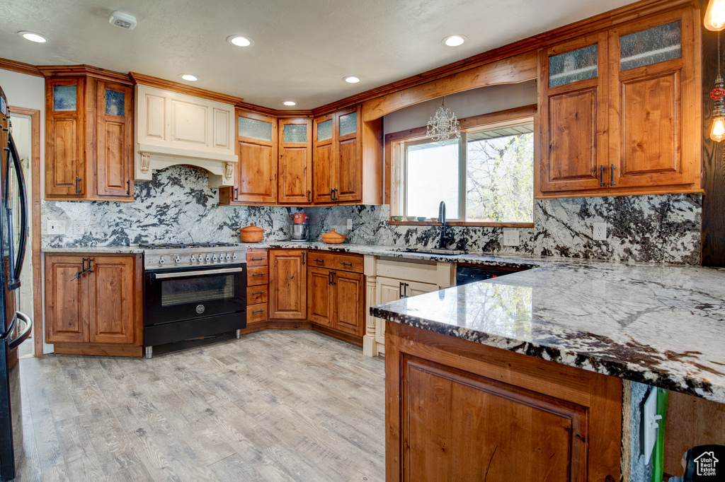 Kitchen featuring range with gas stovetop, backsplash, light hardwood / wood-style flooring, custom exhaust hood, and light stone counters