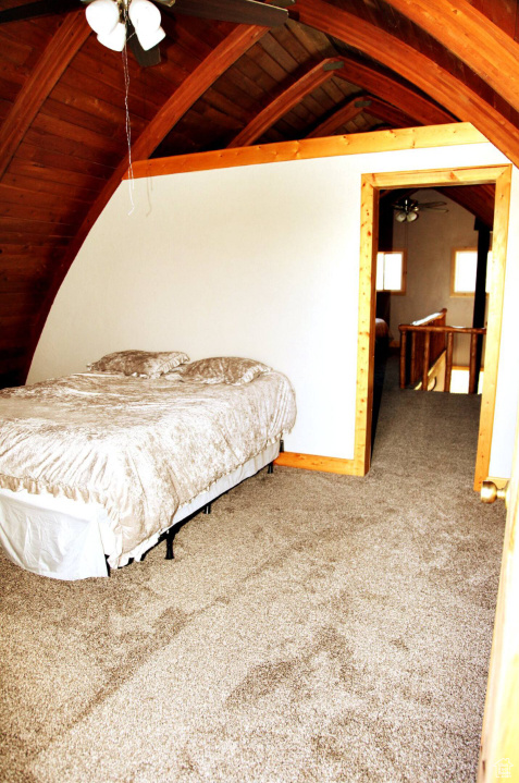Carpeted bedroom featuring lofted ceiling with beams, wooden ceiling, and ceiling fan
