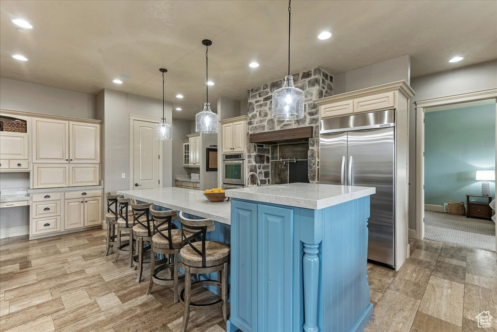 Kitchen featuring pendant lighting, stainless steel appliances, a center island with sink, a kitchen breakfast bar, and light stone countertops