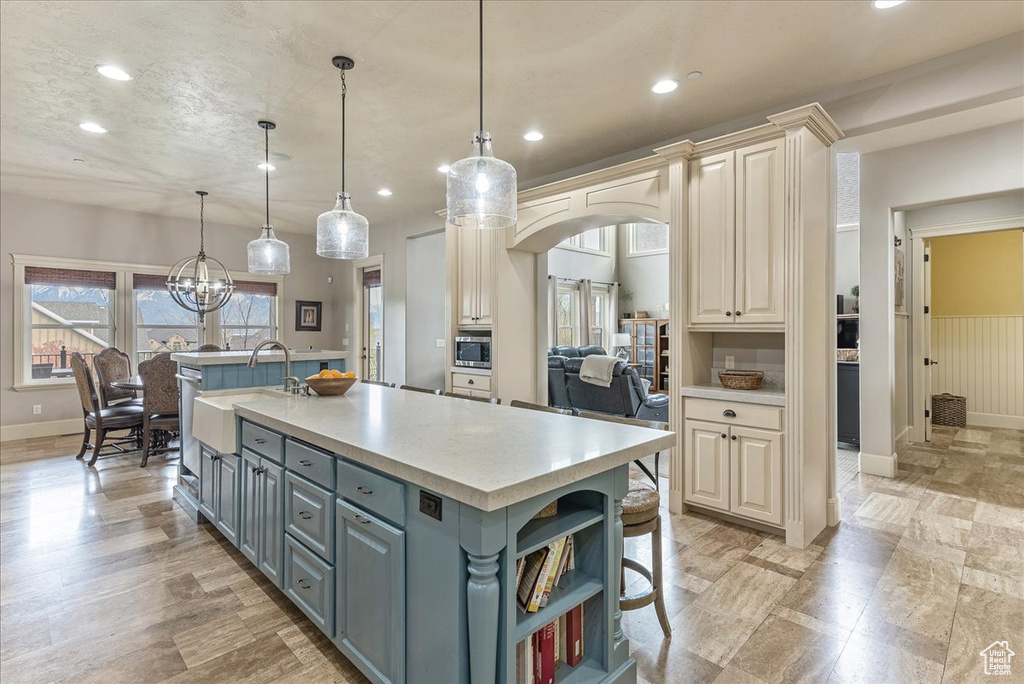 Kitchen with pendant lighting, gray cabinetry, stainless steel microwave, sink, and an island with sink