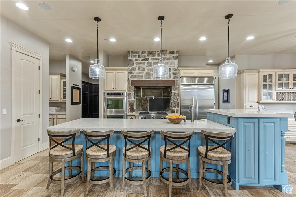 Kitchen featuring a kitchen bar, decorative light fixtures, light hardwood / wood-style flooring, stainless steel appliances, and a kitchen island with sink
