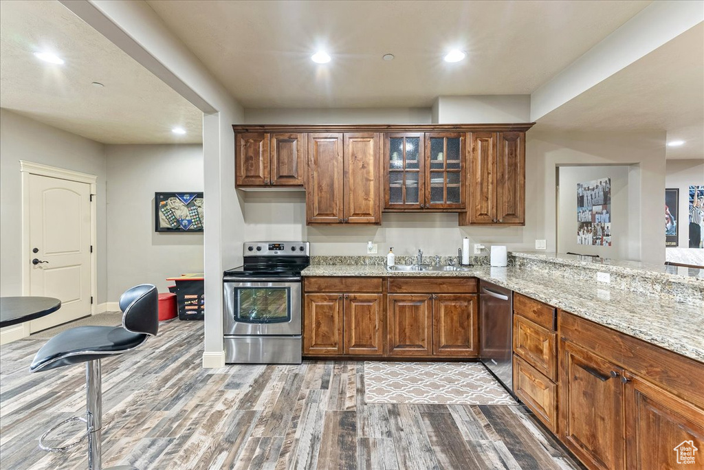Kitchen featuring wood-type flooring, sink, stainless steel appliances, and light stone countertops