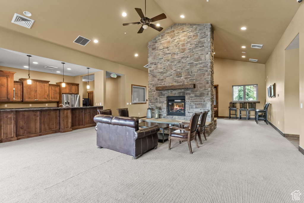 Living room with a stone fireplace, light colored carpet, ceiling fan, and high vaulted ceiling