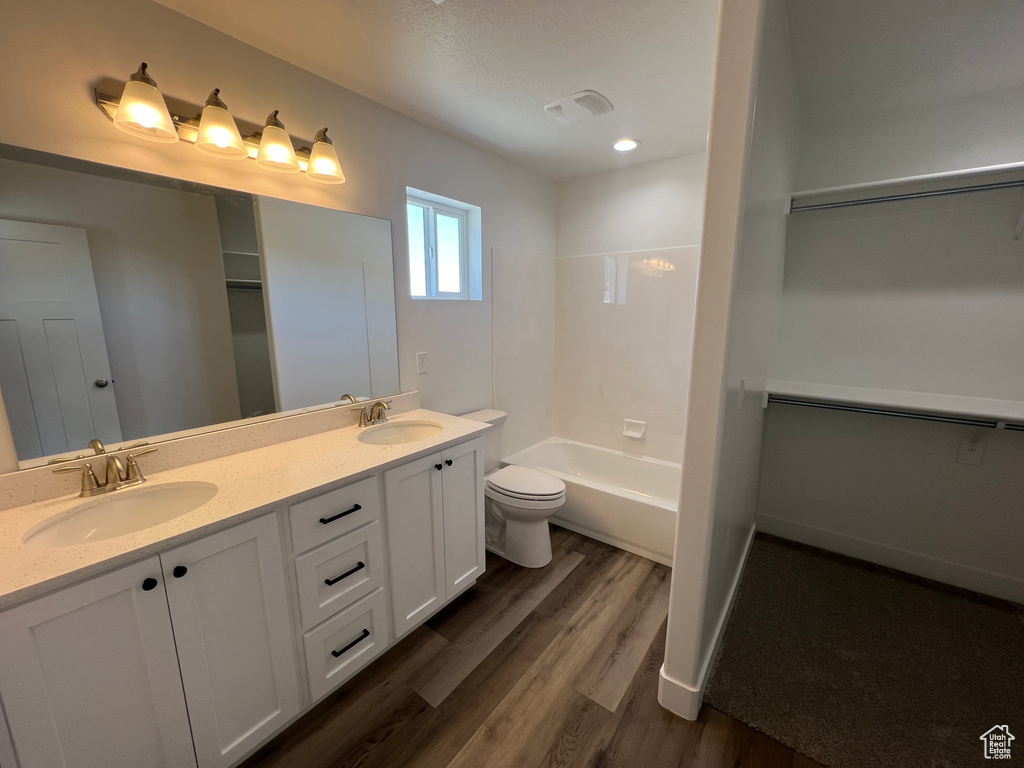 Full bathroom featuring wood-type flooring, large vanity, double sink, bathtub / shower combination, and toilet