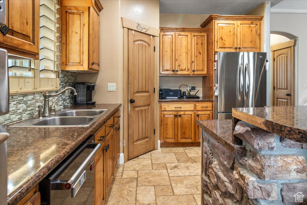 Kitchen with backsplash, stainless steel appliances, light tile flooring, dark stone countertops, and sink