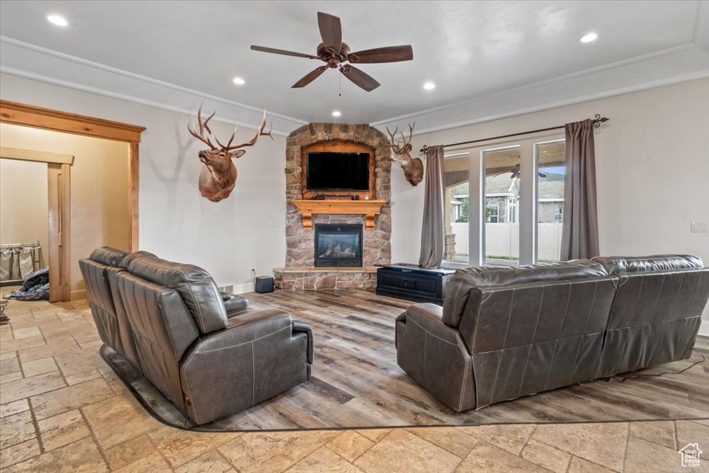 Living room featuring ornamental molding, a stone fireplace, tile flooring, and ceiling fan
