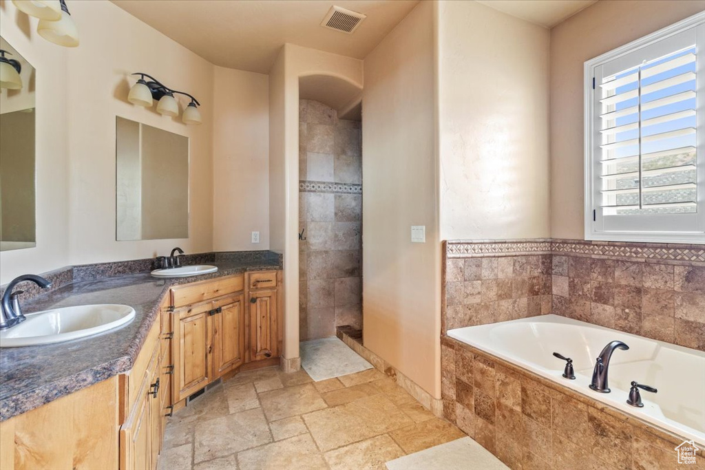 Bathroom featuring tiled tub, dual bowl vanity, a healthy amount of sunlight, and tile floors