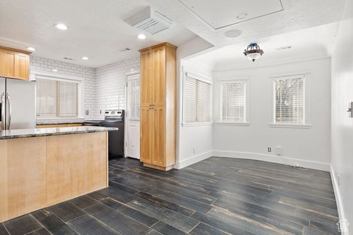 Kitchen with light brown cabinets, dark hardwood / wood-style flooring, dark stone counters, and stainless steel fridge