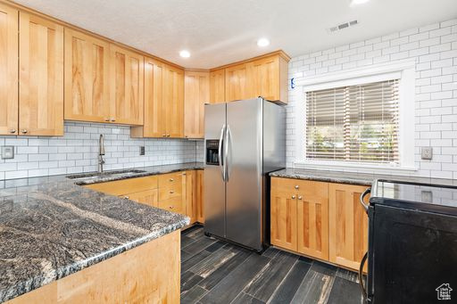 Kitchen featuring stainless steel refrigerator with ice dispenser, tasteful backsplash, dark stone counters, range, and sink
