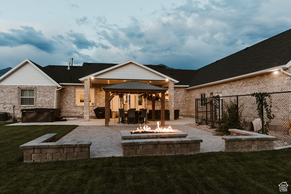 Rear view of house featuring a gazebo, a fire pit, a yard, a hot tub, and a patio area