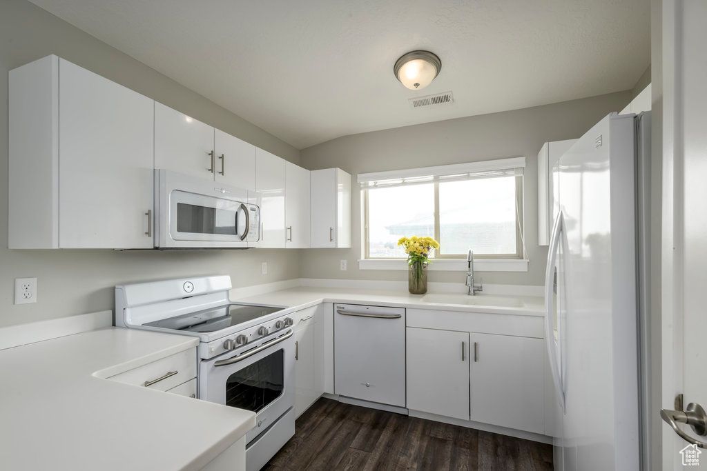 Kitchen featuring white cabinets, dark wood-type flooring, white appliances, and sink