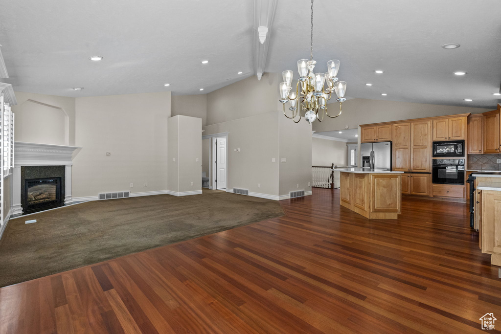Unfurnished living room featuring an inviting chandelier, dark hardwood / wood-style flooring, and high vaulted ceiling