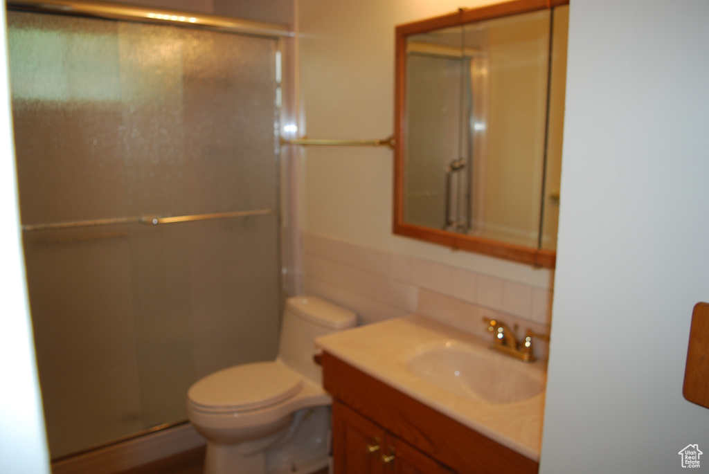 Bathroom featuring a shower with door, toilet, and large vanity