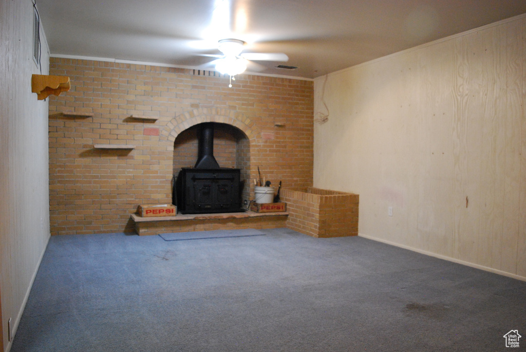 Unfurnished living room with brick wall, dark carpet, ceiling fan, and a wood stove