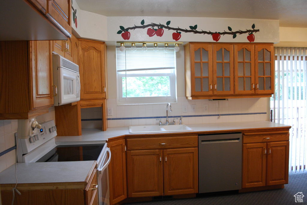 Kitchen with dark colored carpet, plenty of natural light, white appliances, and backsplash
