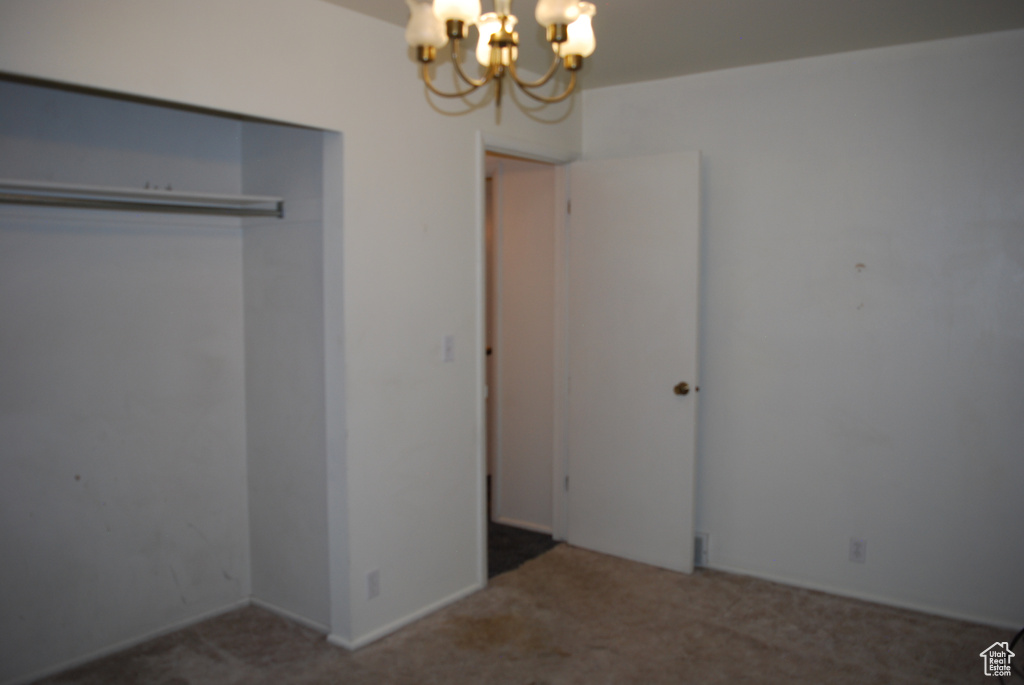 Unfurnished bedroom featuring a closet, dark carpet, and a notable chandelier
