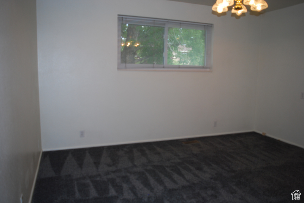 Unfurnished room with dark colored carpet and a chandelier