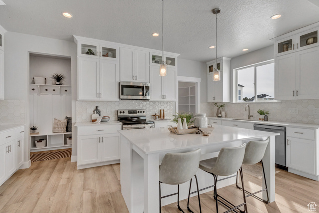Kitchen featuring a kitchen island, white cabinets, tasteful backsplash, light wood-type flooring, and stainless steel appliances