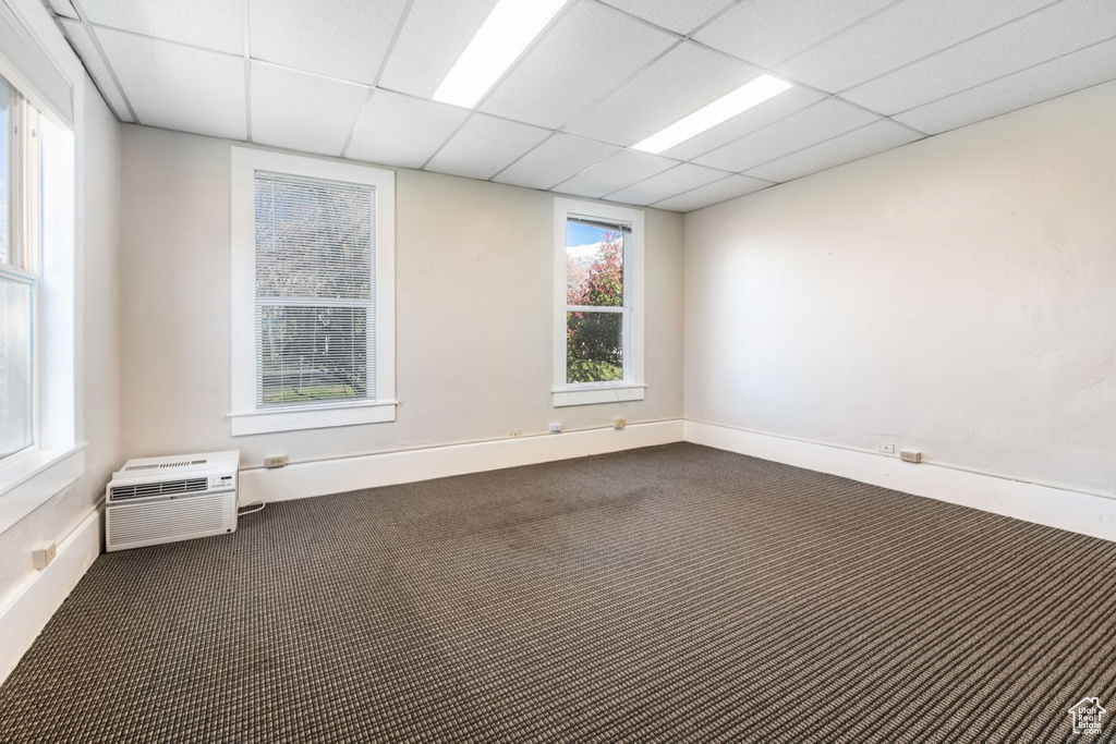 Empty room with a drop ceiling, a wall mounted AC, and dark colored carpet