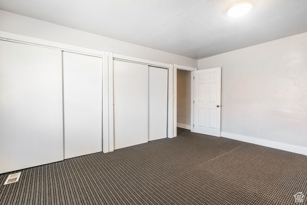 Unfurnished bedroom featuring dark carpet and multiple closets