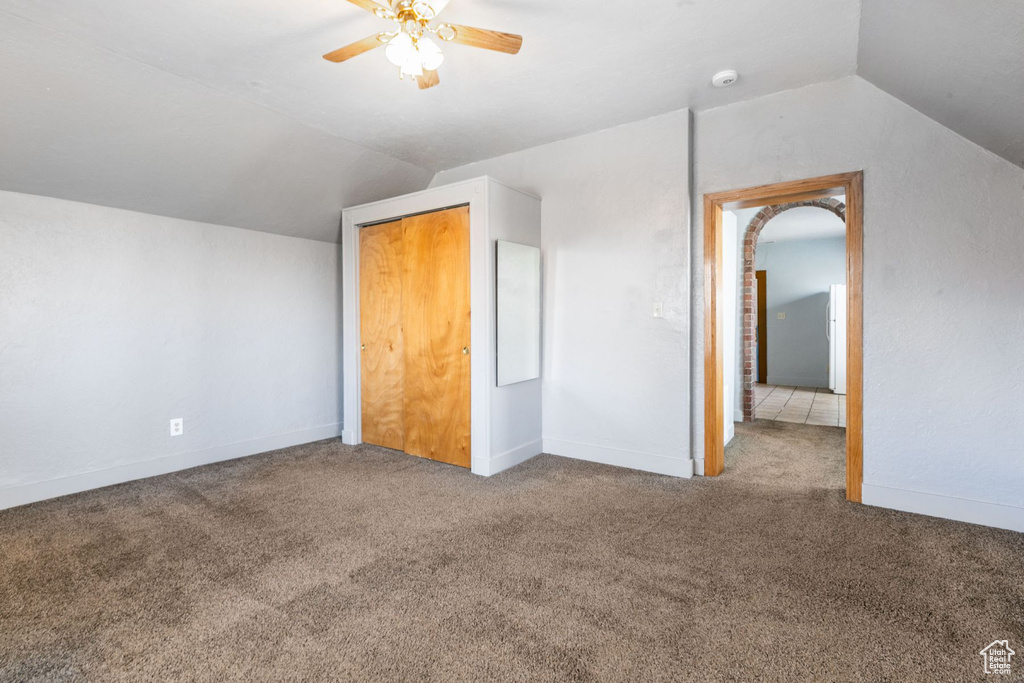 Interior space with a closet, dark carpet, ceiling fan, and vaulted ceiling