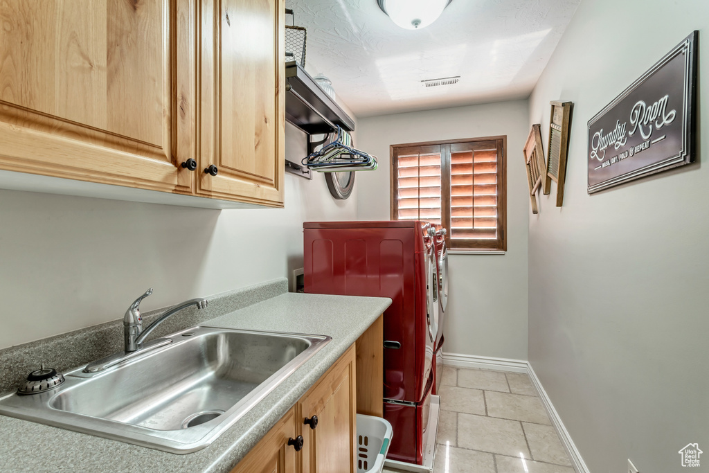 Laundry room featuring sink, washer and clothes dryer, cabinets, and light tile floors