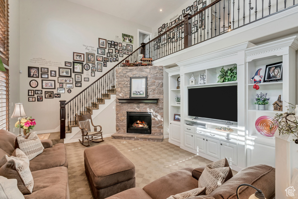 Living room with light colored carpet, a high ceiling, a stone fireplace, and built in shelves