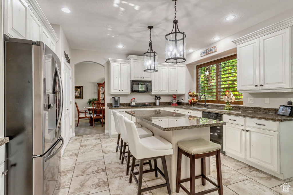 Kitchen featuring light tile floors, a kitchen island, dark stone counters, black appliances, and a kitchen breakfast bar