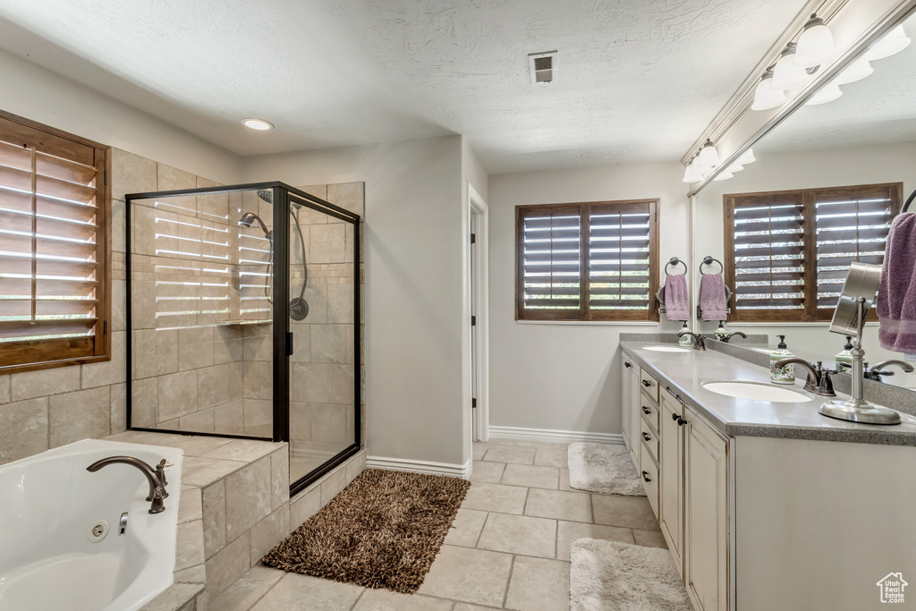 Bathroom featuring tile floors, shower with separate bathtub, dual vanity, and a textured ceiling