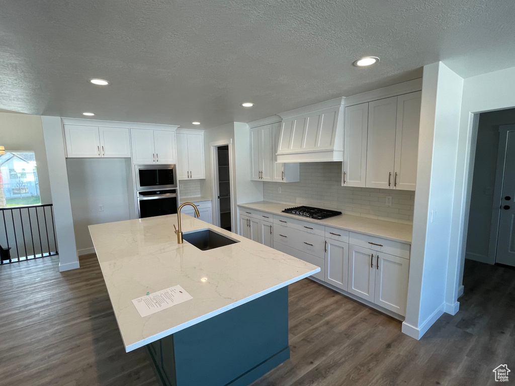 Kitchen with custom exhaust hood, white cabinets, sink, dark hardwood / wood-style flooring, and an island with sink