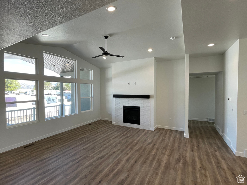 Unfurnished living room with lofted ceiling, dark hardwood / wood-style flooring, ceiling fan, and a fireplace