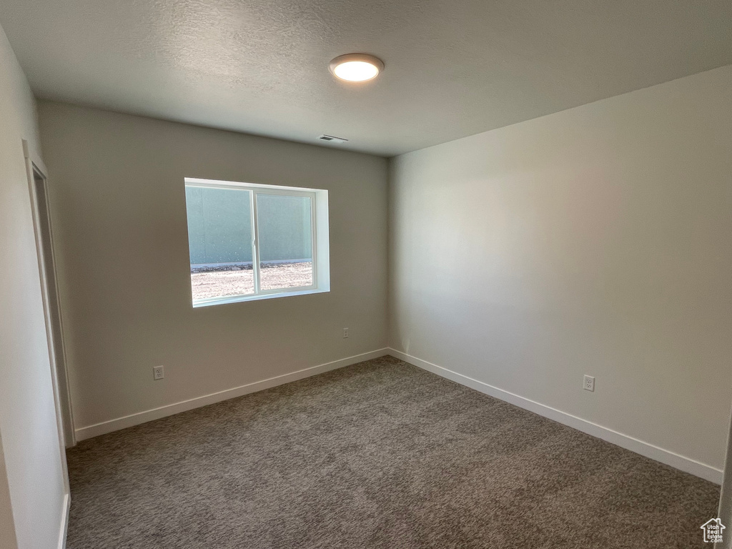 Unfurnished room featuring a textured ceiling and dark colored carpet