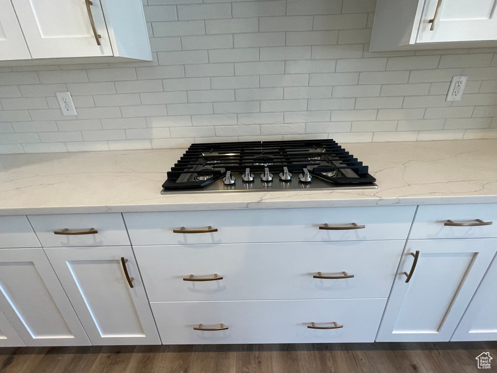 Kitchen featuring backsplash, dark wood-type flooring, light stone countertops, and white cabinets