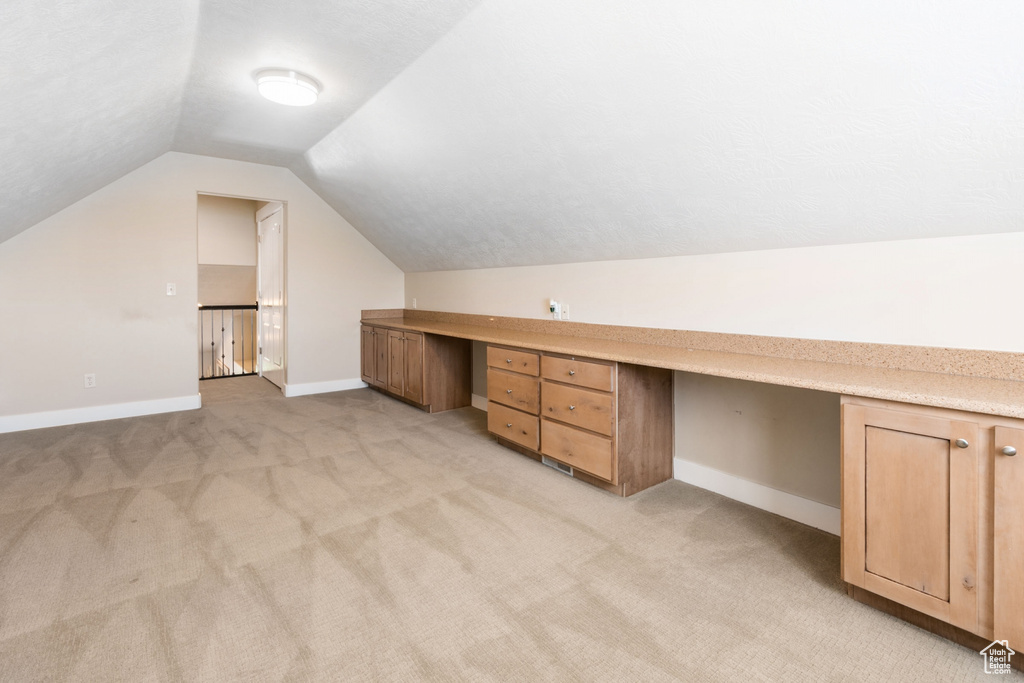 Bonus room featuring lofted ceiling, built in desk, and light carpet