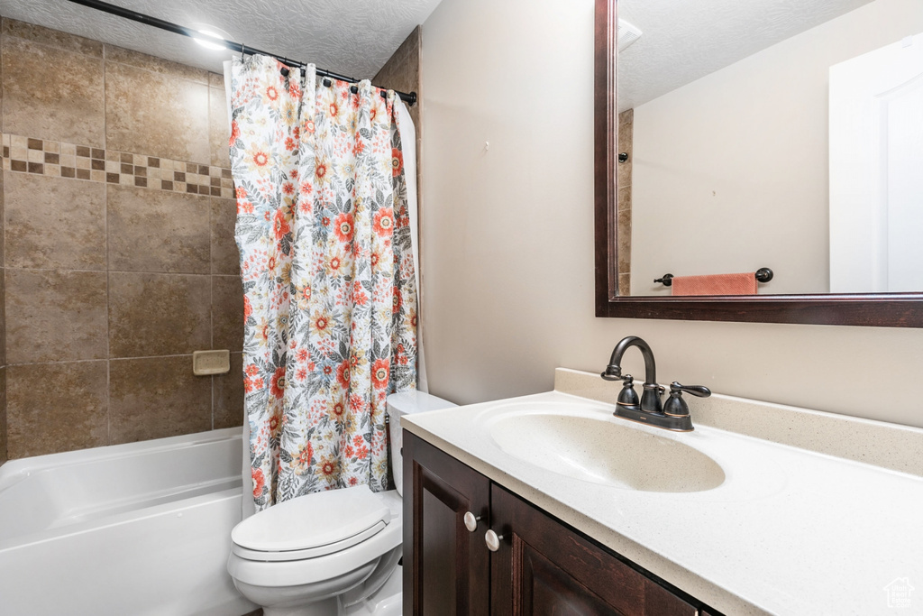 Full bathroom with shower / bathtub combination with curtain, vanity, toilet, and a textured ceiling