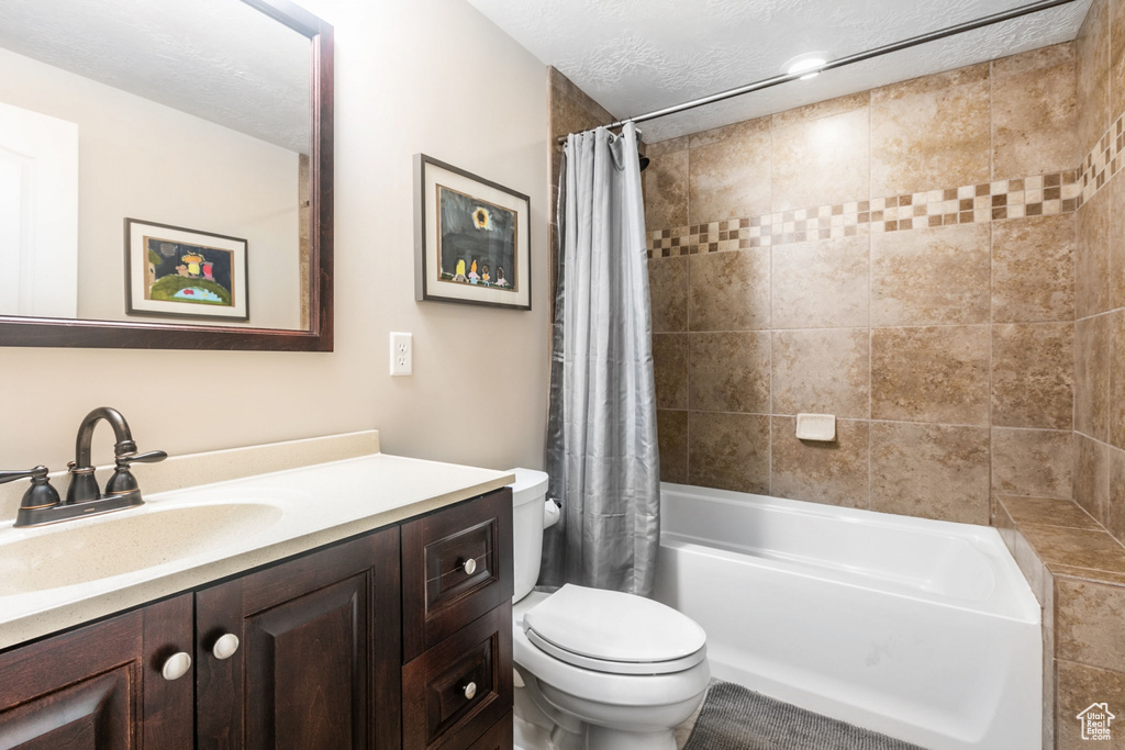 Full bathroom with vanity with extensive cabinet space, toilet, shower / tub combo with curtain, and a textured ceiling
