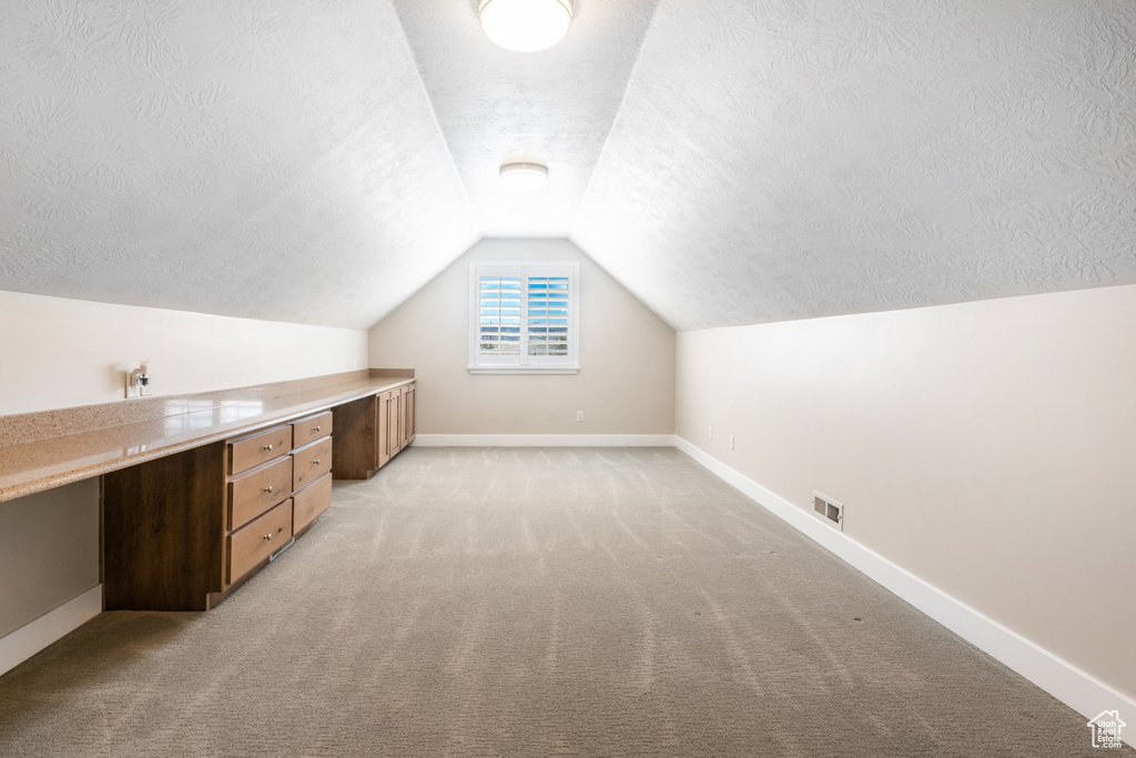 Bonus room with light colored carpet, lofted ceiling, built in desk, and a textured ceiling