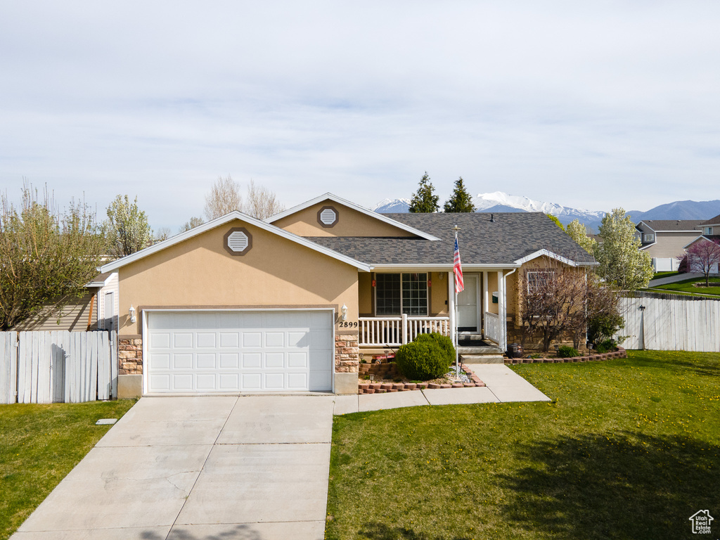 Ranch-style home with a garage, a mountain view, covered porch, and a front lawn