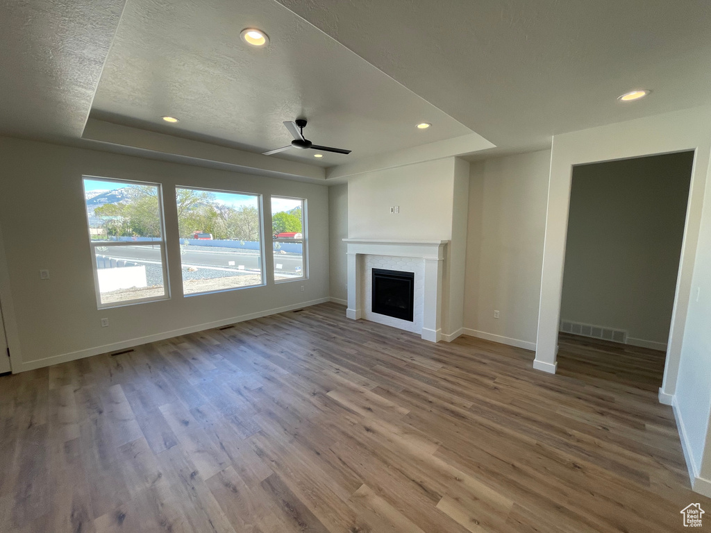 Unfurnished living room with hardwood / wood-style flooring, a textured ceiling, ceiling fan, and a raised ceiling