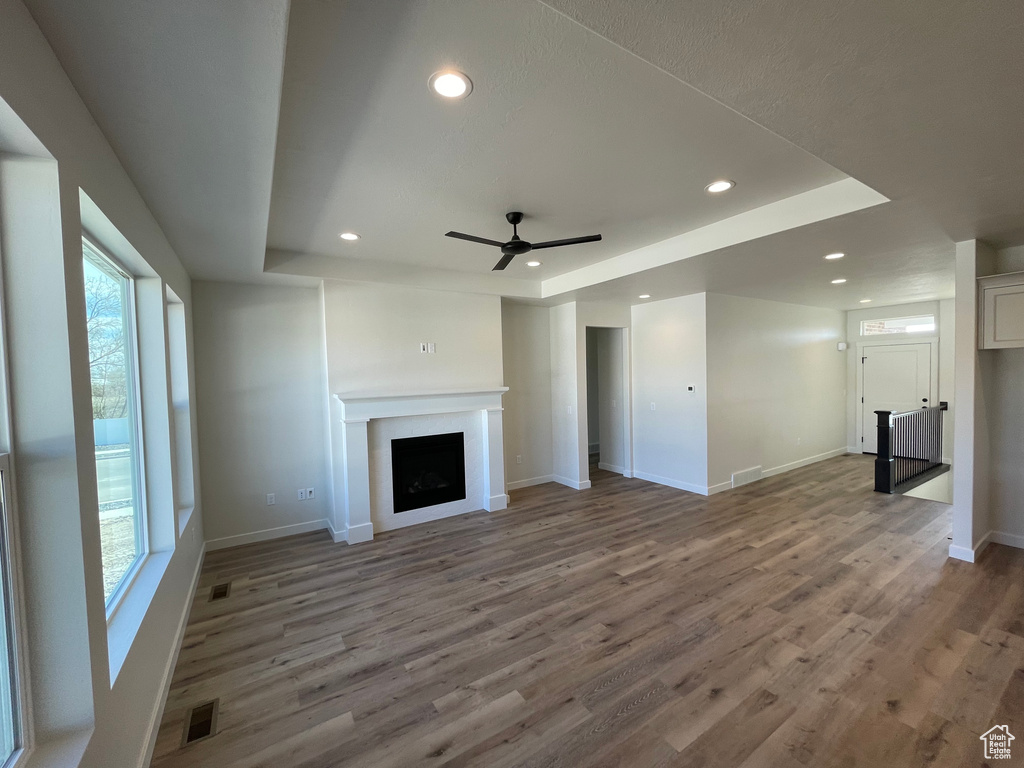Unfurnished living room featuring wood-type flooring, plenty of natural light, ceiling fan, and a tray ceiling