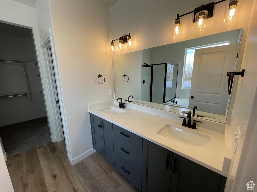 Bathroom featuring hardwood / wood-style flooring, double sink, a shower with shower door, and vanity with extensive cabinet space
