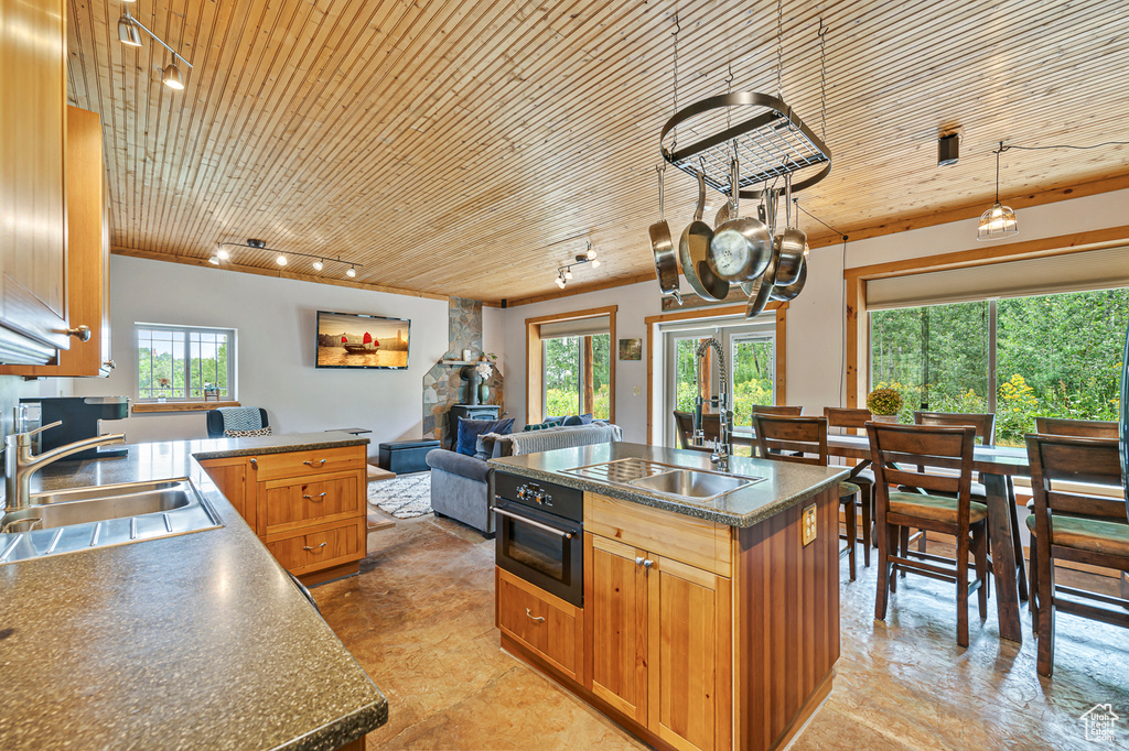 Kitchen with oven, sink, wood ceiling, decorative light fixtures, and an island with sink