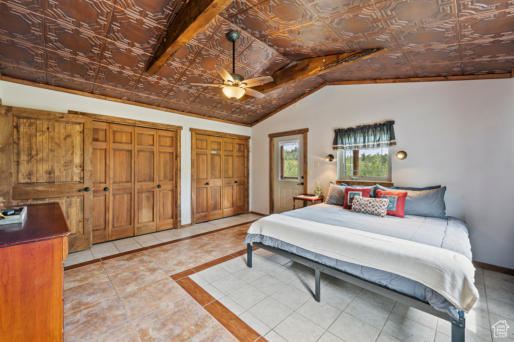 Tiled bedroom featuring ceiling fan, vaulted ceiling, and multiple closets