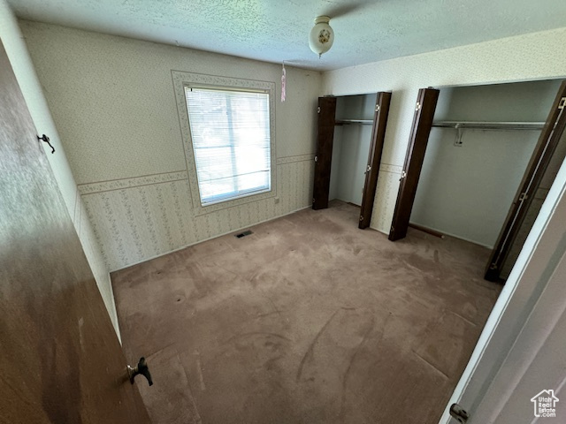 Unfurnished bedroom with carpet flooring, a textured ceiling, and multiple closets