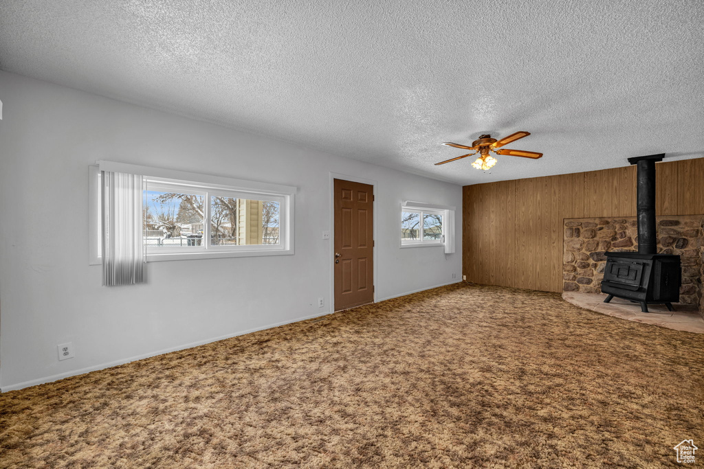Unfurnished living room featuring carpet flooring, ceiling fan, a textured ceiling, and a wood stove