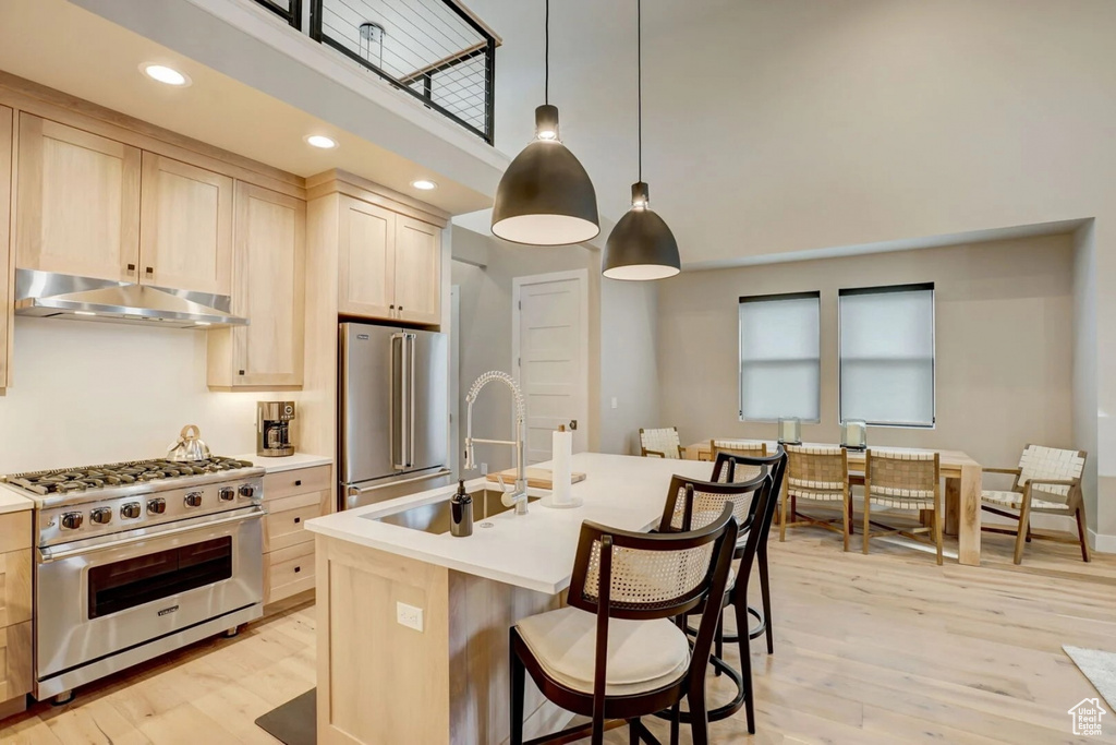 Kitchen featuring high end appliances, decorative light fixtures, light hardwood / wood-style flooring, a towering ceiling, and an island with sink