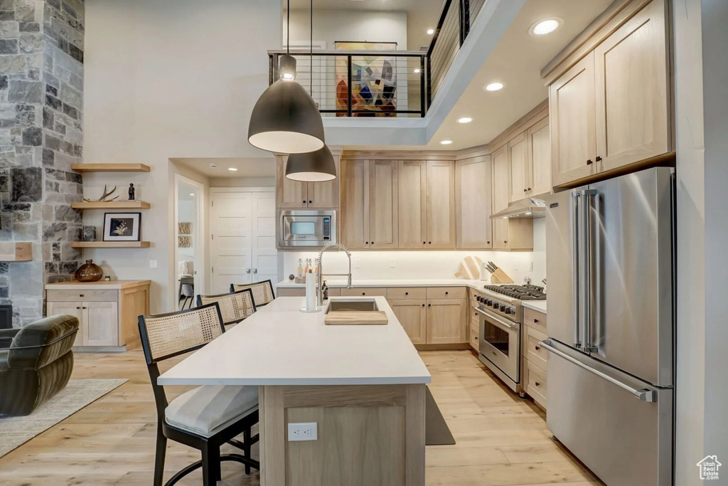 Kitchen featuring light hardwood / wood-style floors, a high ceiling, premium appliances, light brown cabinetry, and pendant lighting